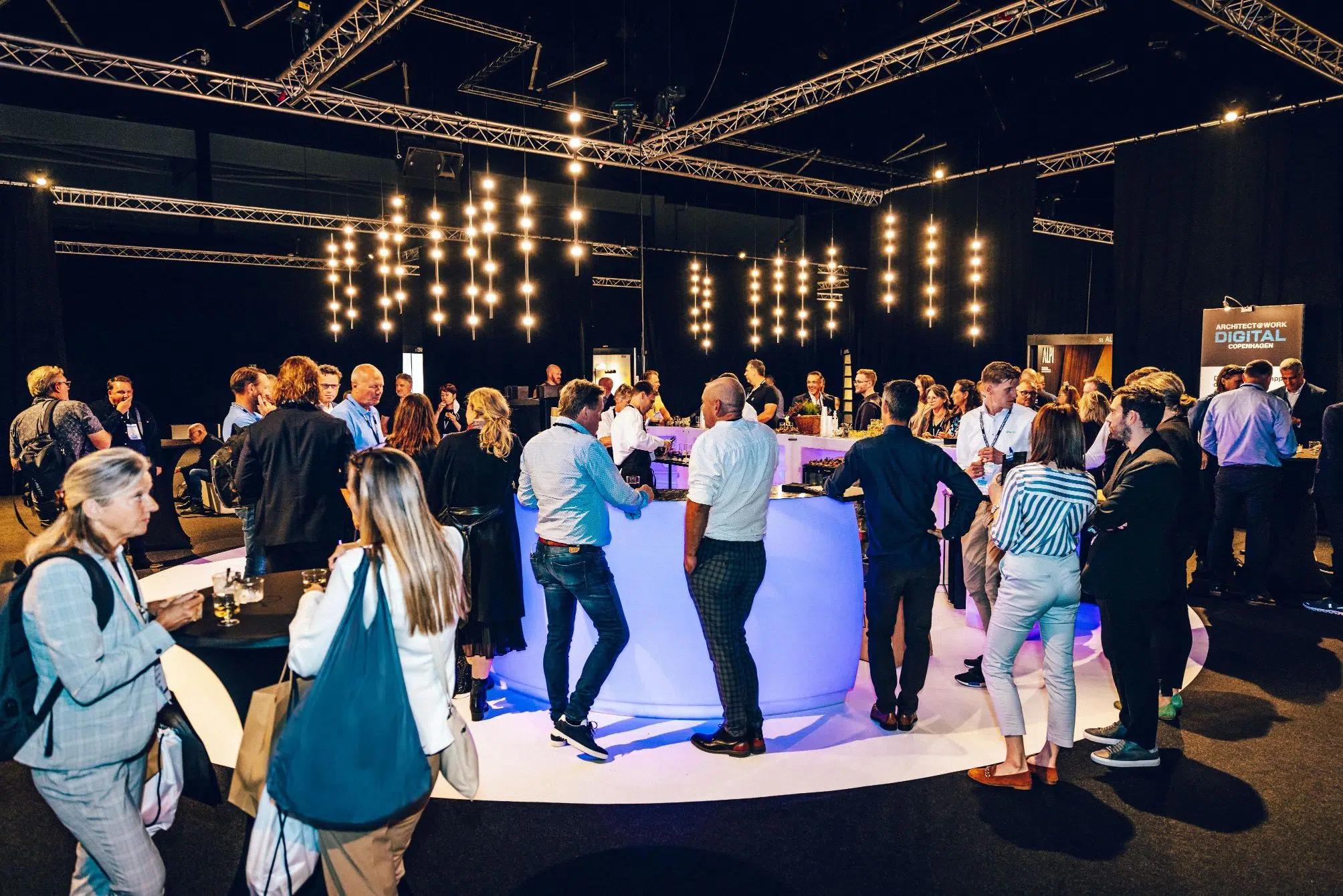 Networking event with professionals engaging around a stylish bar area, illuminated by pendant lights.