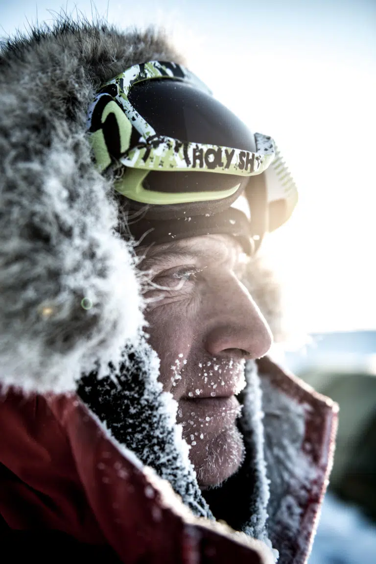 Close-up of a man with frost on his face and wearing goggles in a snowy environment.
