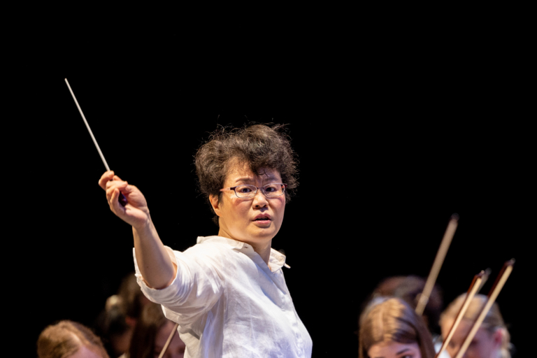 Frau Dirigentin mit einem Taktstock vor einem Orchester