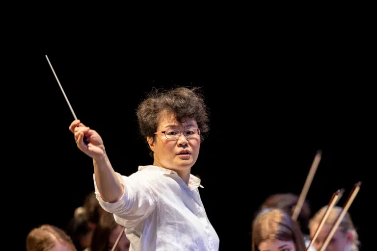 Frau Dirigentin mit einem Taktstock vor einem Orchester