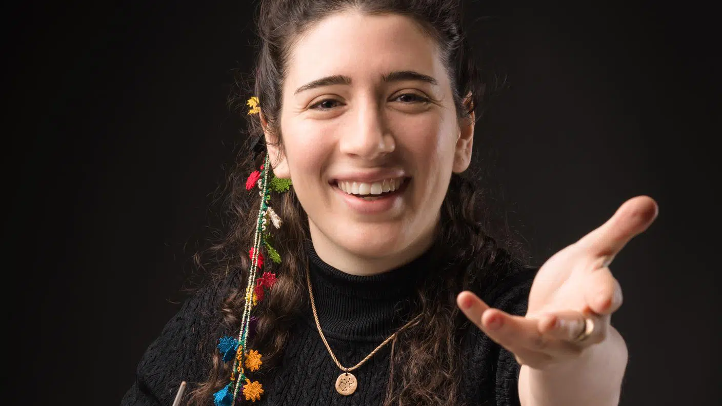 Junge Frau mit lockigen Haaren und buntem Schmuck, die lächelt und ihre Hand ausstreckt.